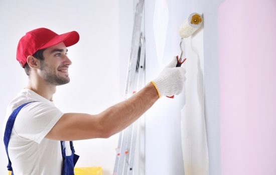 Young worker painting wall in room